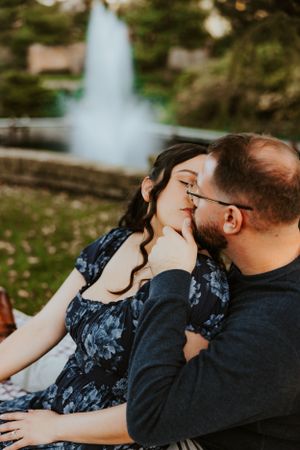 A romantic couple sharing an intimate moment by a fountain in a park during autumn.