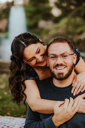 A joyful couple shares an intimate moment outdoors during sunset, with the woman embracing from behind.