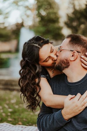 A romantic couple share a tender kiss outdoors on a sunny day with soft bokeh lighting in the background.