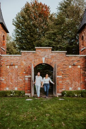 Old brick archway entrance with herringbone pattern brickwork and surrounding autumn trees on a grassy lawn.