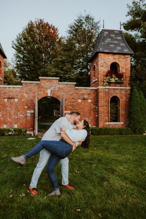 A romantic moment shared outdoors in front of brick archways and towers during autumn.