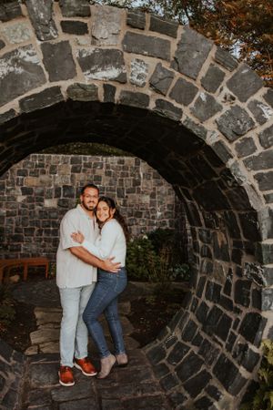 A couple embraces under a stone archway in a romantic outdoor portrait setting at dusk.