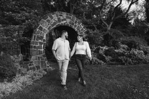 A couple walks through a stone archway in a garden, captured in black and white photography.