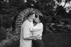 A romantic black and white moment between two figures embracing in front of a stone archway outdoors.