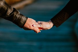 Two hands gently holding each other against a blurred teal background in an intimate moment of connection.