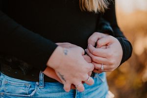 Close-up shot of hands resting on denim jeans waistband in golden sunlight.