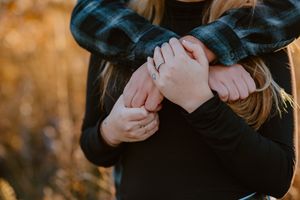 Close-up of hands crossed over chest wearing a black sweater in warm autumn sunlight.