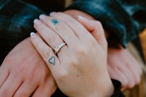 Close up of a hand wearing an engagement ring and delicate heart tattoo on the finger.