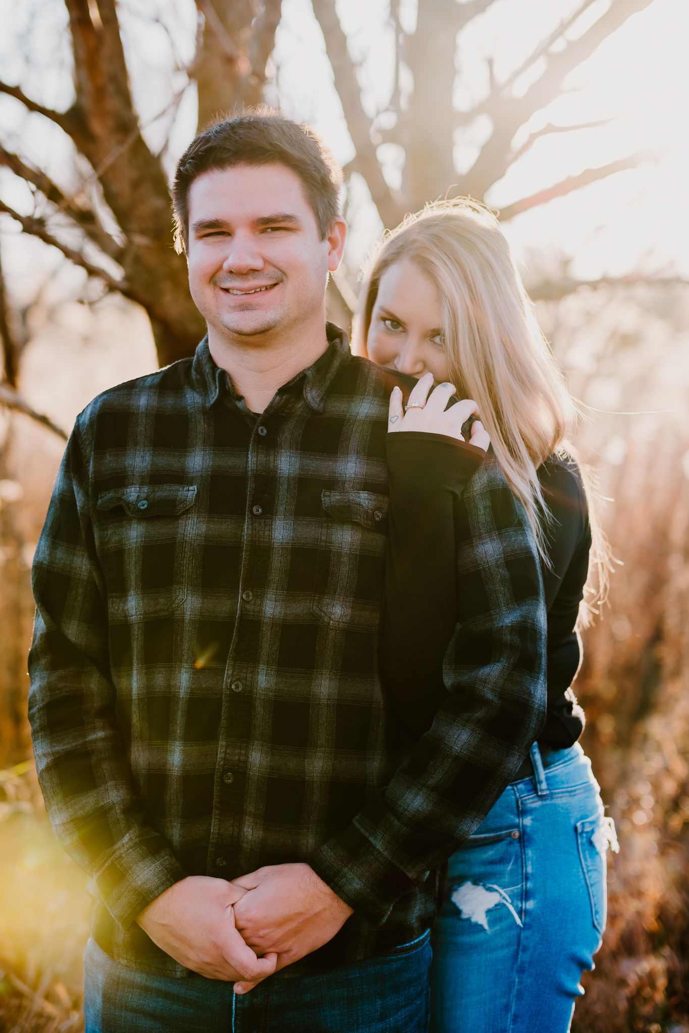 A couple poses together outdoors during golden hour sunset with trees in background.