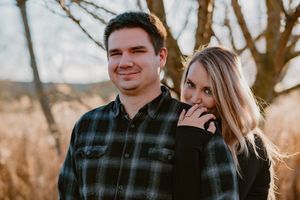 A couple poses together outdoors during golden hour, with one wearing a plaid flannel shirt.