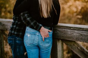 Person in jeans and plaid shirt leaning against wooden railing with autumn colors in background.