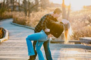 Couple embraces in romantic dance pose on wooden boardwalk during golden hour sunset.