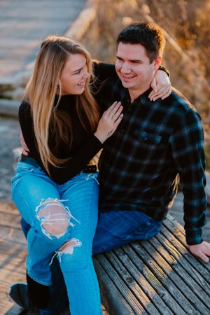 A couple sitting together on a wooden dock during golden hour, sharing an intimate moment and laughter.
