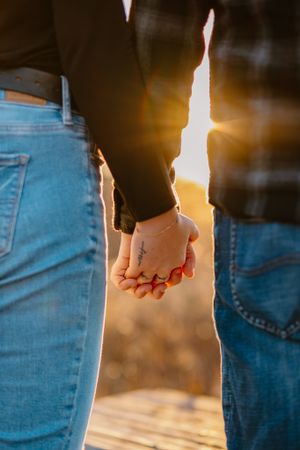 Two people holding hands at sunset, with a small tattoo visible on one person's hand.