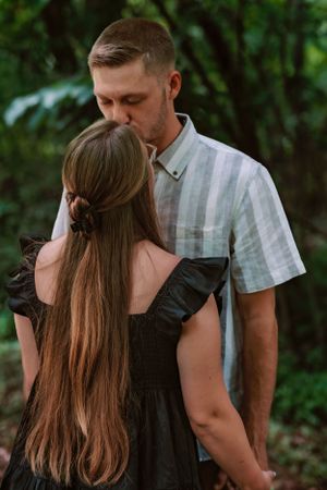A romantic couple shares an intimate moment in a garden setting, with her long brown hair and black dress visible.
