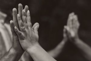 Hands raised together in a group high five celebration gesture against dark background.