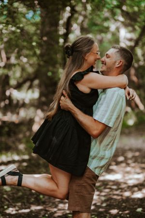 A joyful couple embraces and laughs together in a sunlit forest setting.