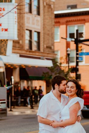A couple in white outfits share an intimate moment on a city street corner during golden hour.