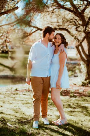 A couple embraces in a romantic outdoor setting with sunlit trees and soft bokeh lighting during golden hour.