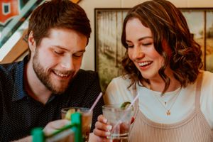 Two people share a laugh while drinking cocktails together in an intimate setting.