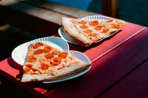 Two slices of pepperoni pizza on white paper plates resting on a red surface.