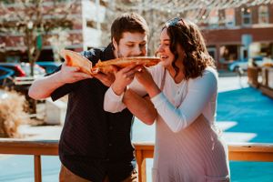A joyful couple sharing pizza together on a sunny outdoor patio during a casual dining experience.