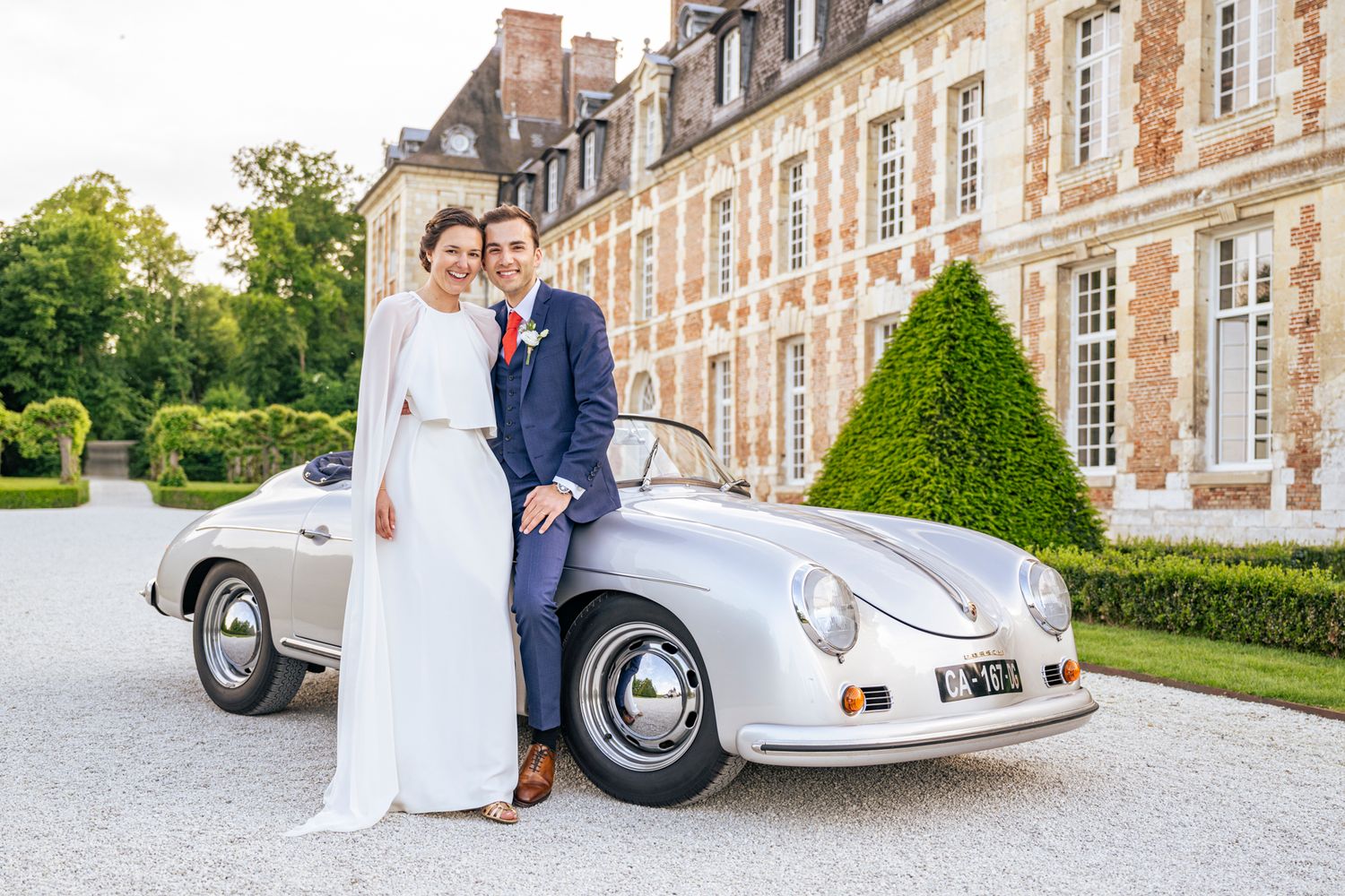 Elegant wedding portrait with classic Porsche at a grand chateau.