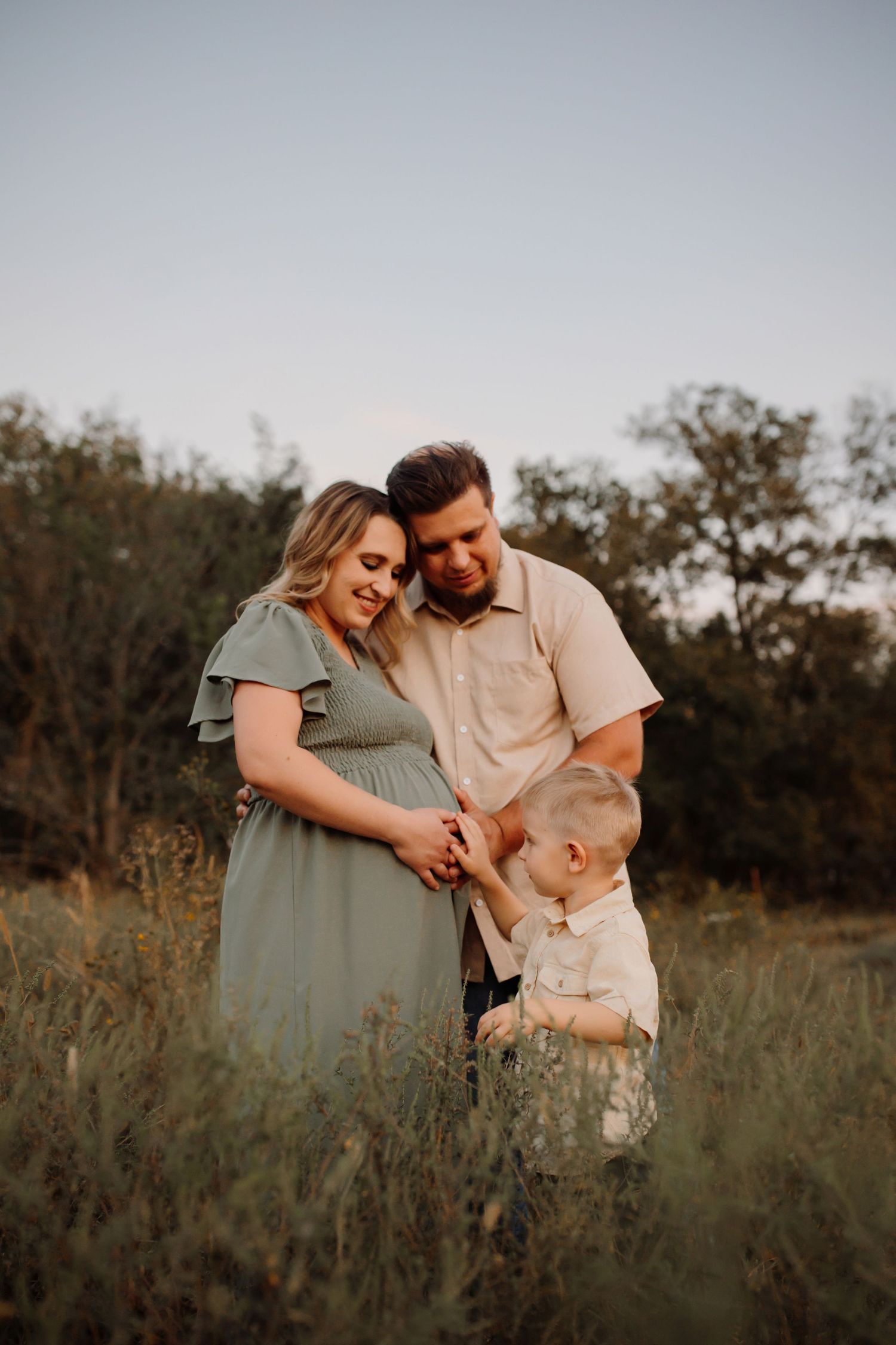A pregnant person in a white top and rust skirt holds dried flowers against their belly during an outdoor maternity photoshoot.