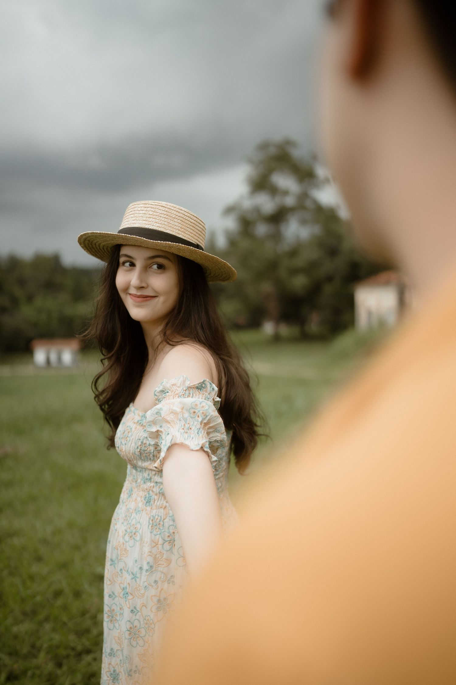 A dreamy romantic photoshoot in a field features floral dress and straw hat.