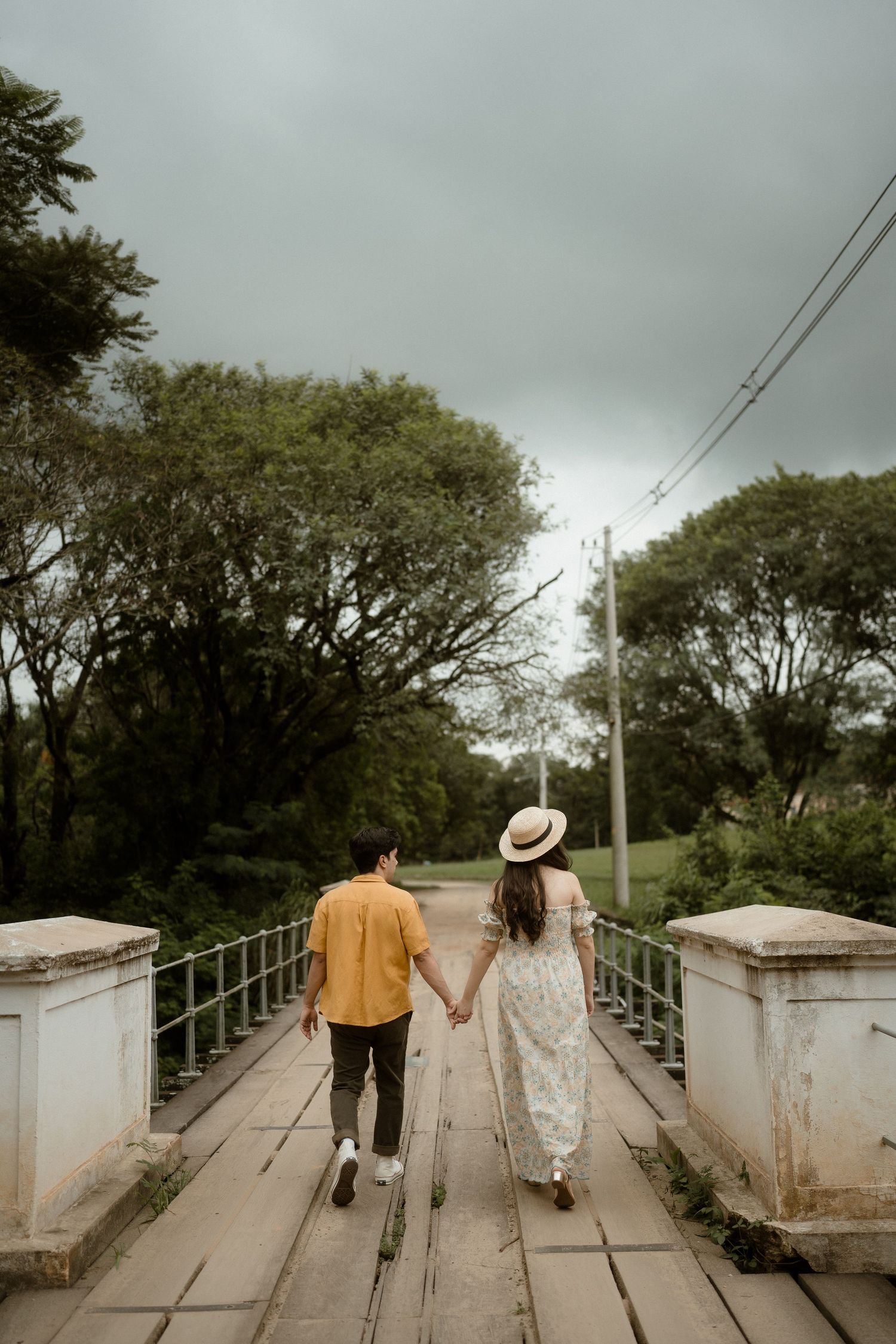 A couple walks along a picturesque bridge under moody skies.