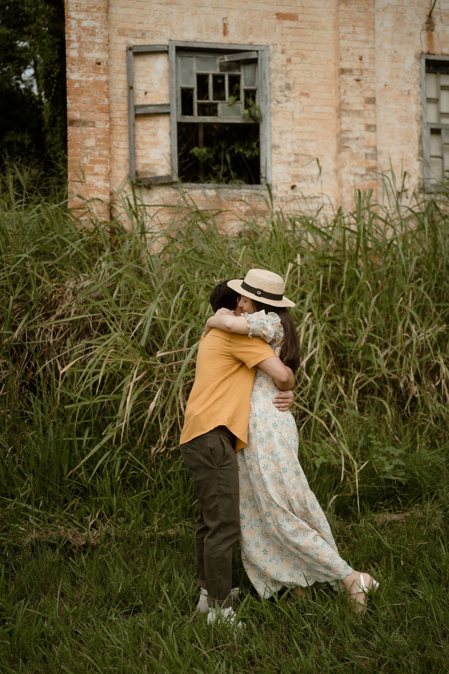 Romantic embrace captured against abandoned building and wild grass.