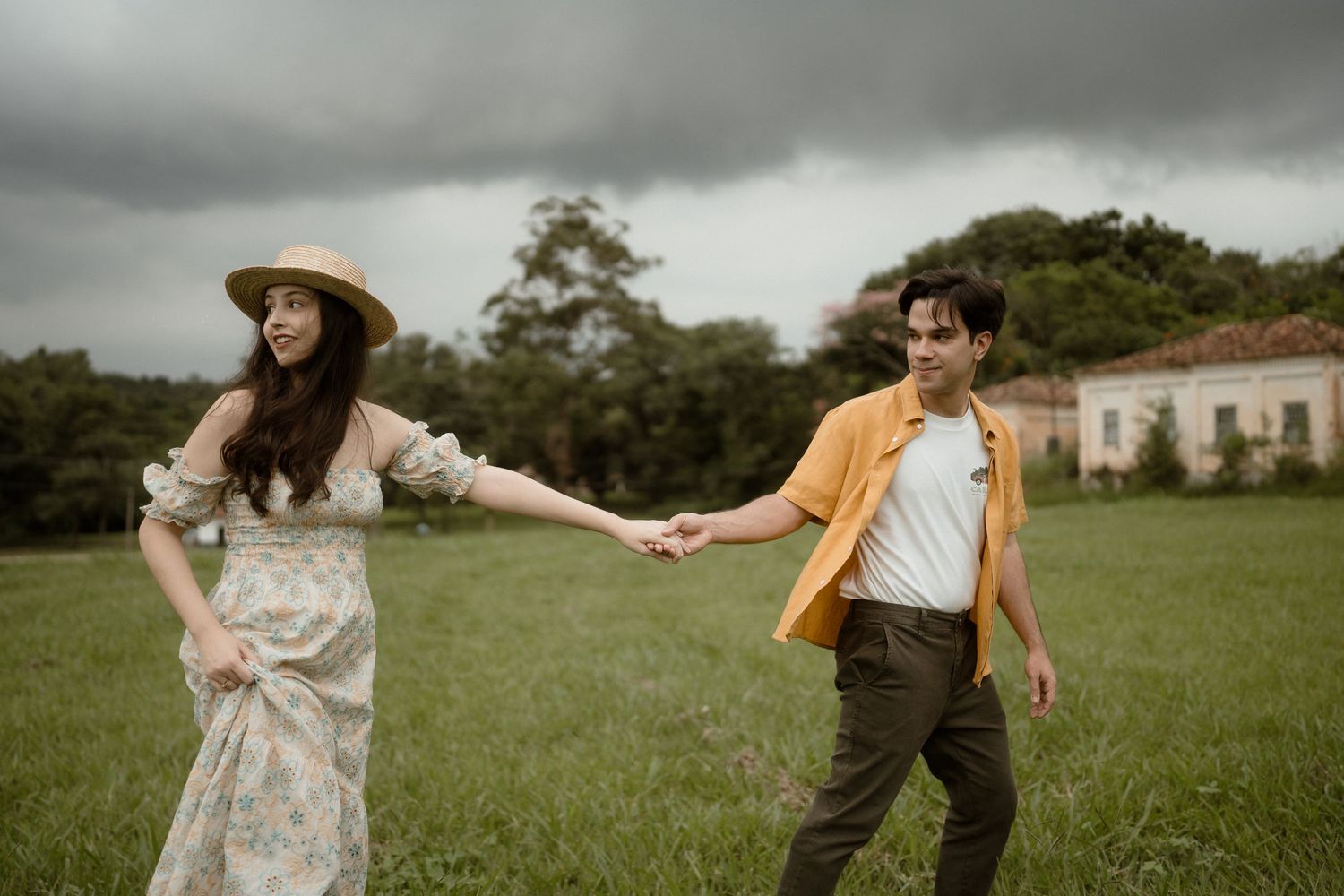 Two people in vintage attire dance playfully in a grassy field.