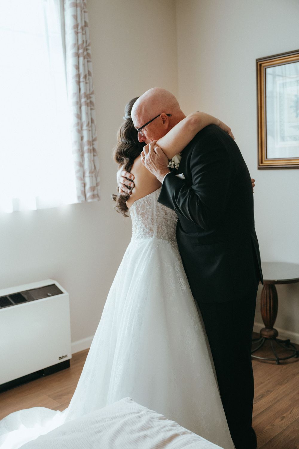 A bride and her father share an emotional embrace in a bright room before her wedding ceremony.