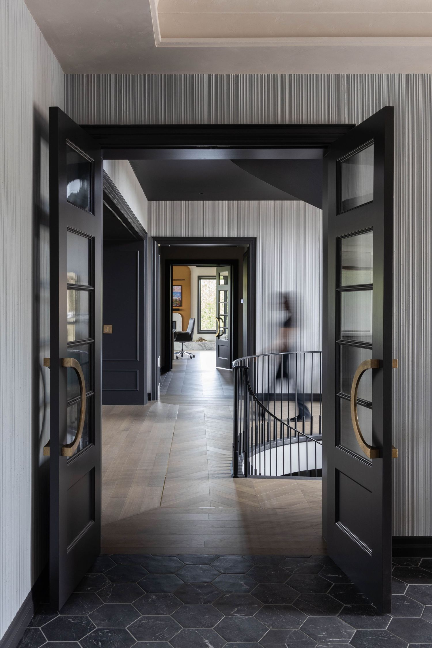 Elegant hallway with black double doors, gold handles, hexagonal tile floors, and striped wallpaper leading to a bright corridor.