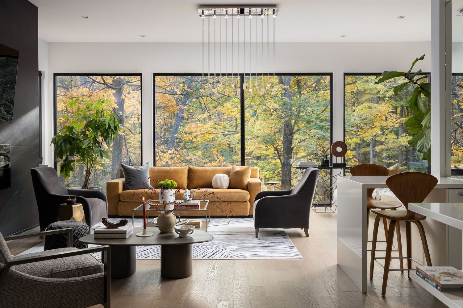 Modern living room with floor-to-ceiling windows, amber sofa, and autumn forest views.