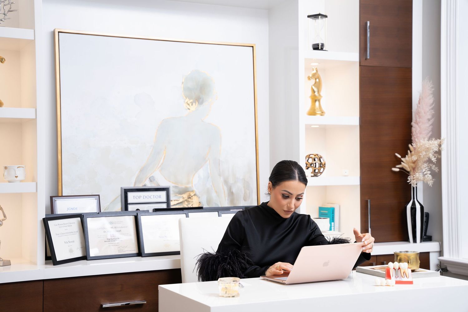 A person in black attire working on a laptop in a modern office space with white decor and framed artwork.