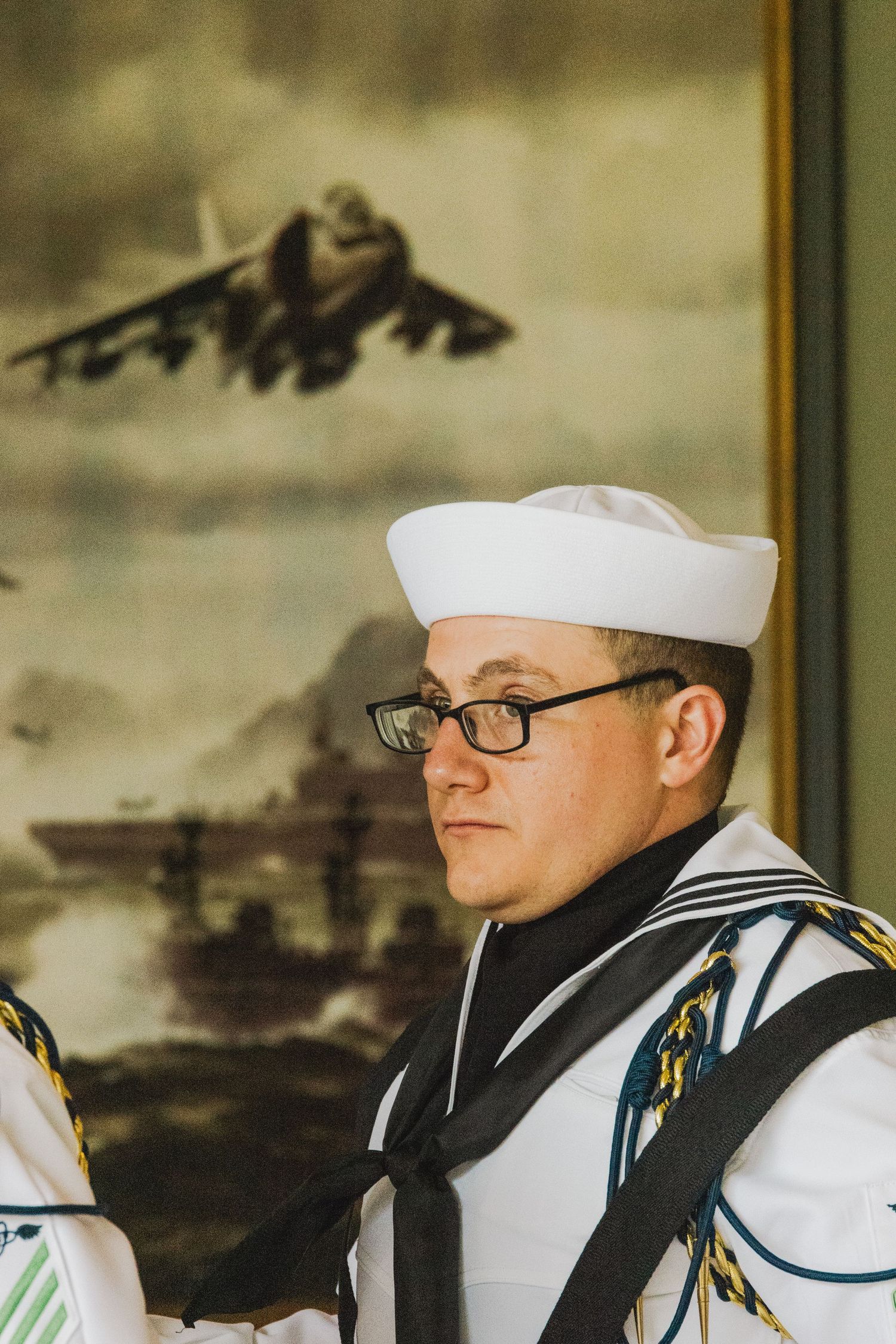Professional military portrait photography of a U.S. Navy Sailor in Dress Whites standing at attention before a naval aviation painting.