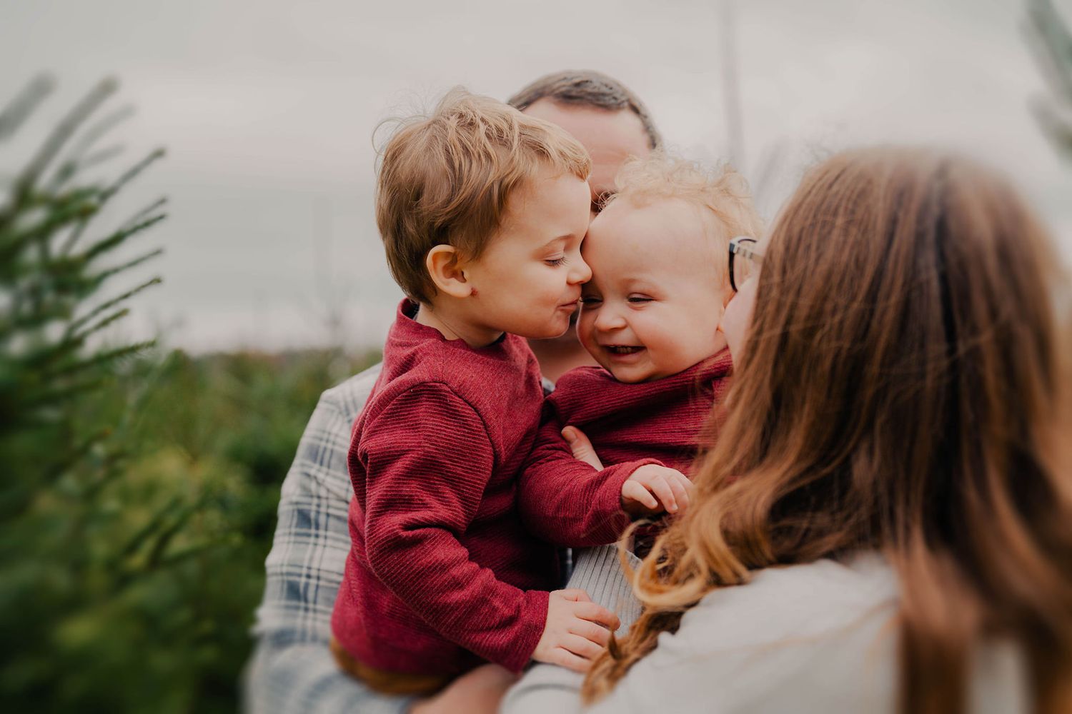 Intimate family moment captured outdoors with natural lighting and greenery.