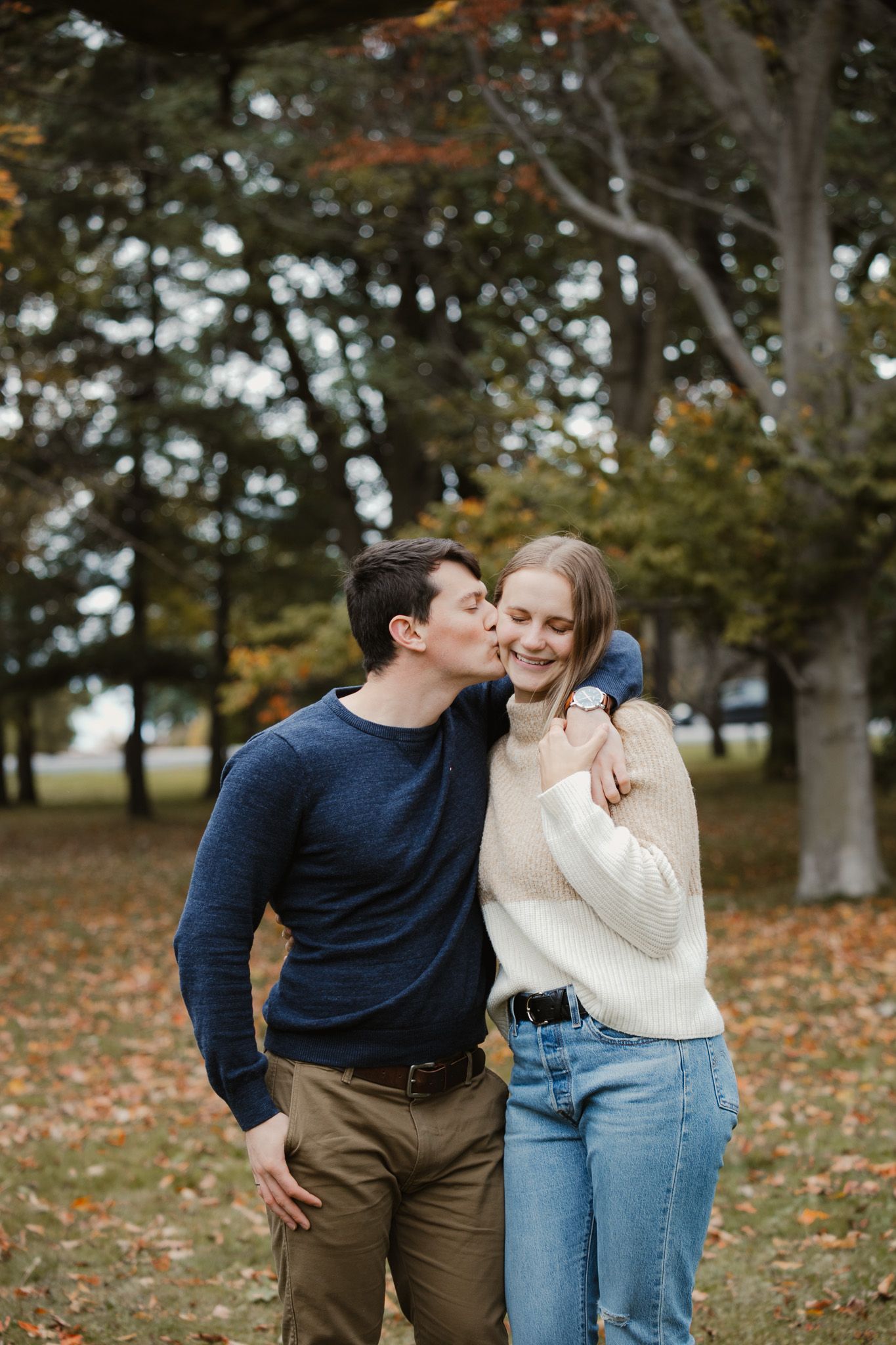 A romantic autumn engagement photo of a couple embracing outdoors among fallen leaves.