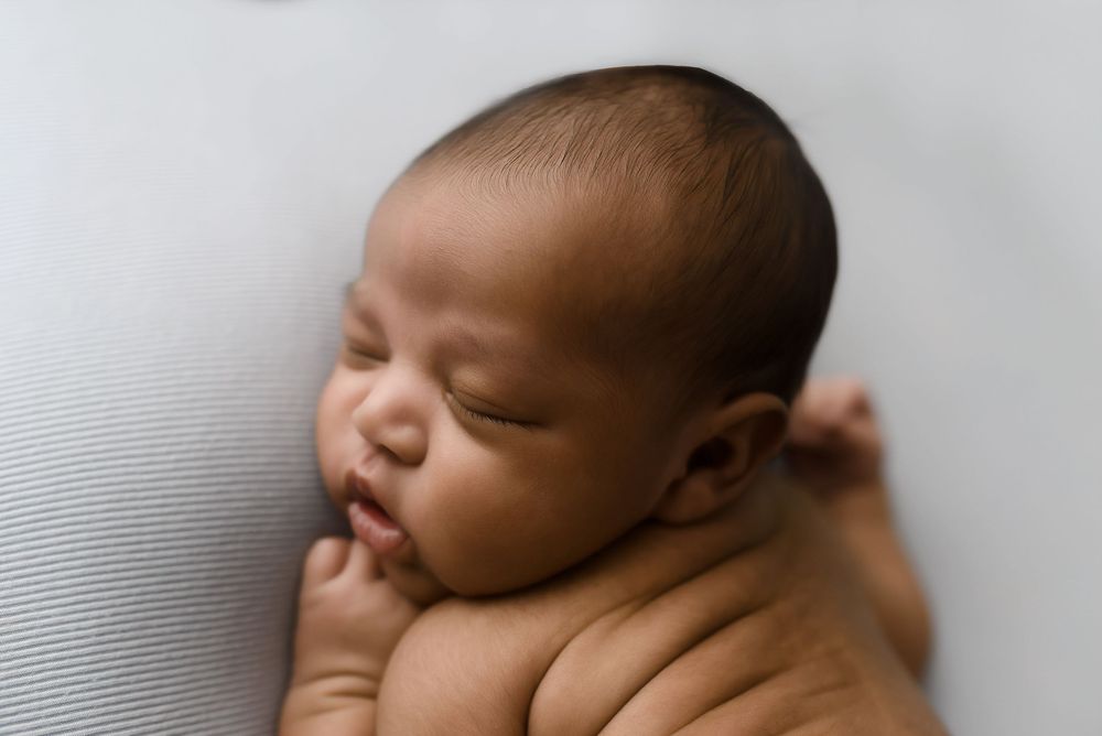 Peaceful sleeping newborn baby with dark hair resting on a soft white blanket in a serene portrait.