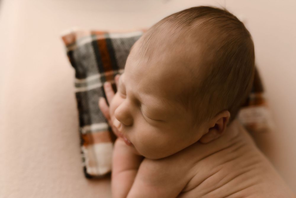 Peaceful newborn baby sleeping on a soft beige blanket beside a plaid fabric in warm tones.