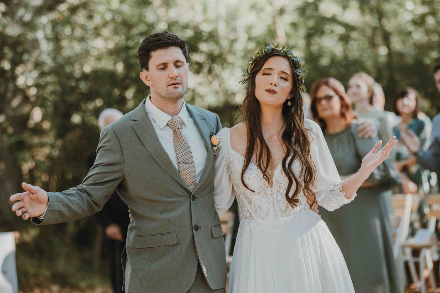 Bride and groom sharing a joyful outdoor wedding ceremony moment, bride in floral crown and white gown, groom in gray suit.