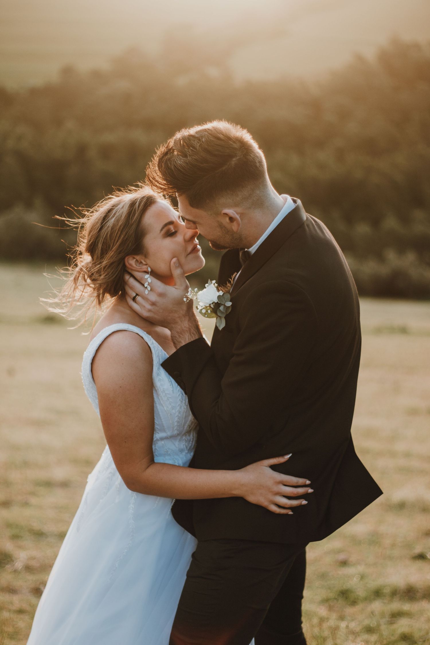 A bride and groom share a romantic moment at golden hour in a sunlit field, the bride in a light blue dress.