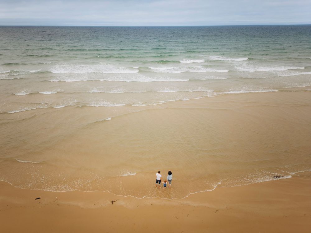 Panoramic view of sandy beach with gentle waves rolling onto shore and distant ocean horizon under cloudy sky.