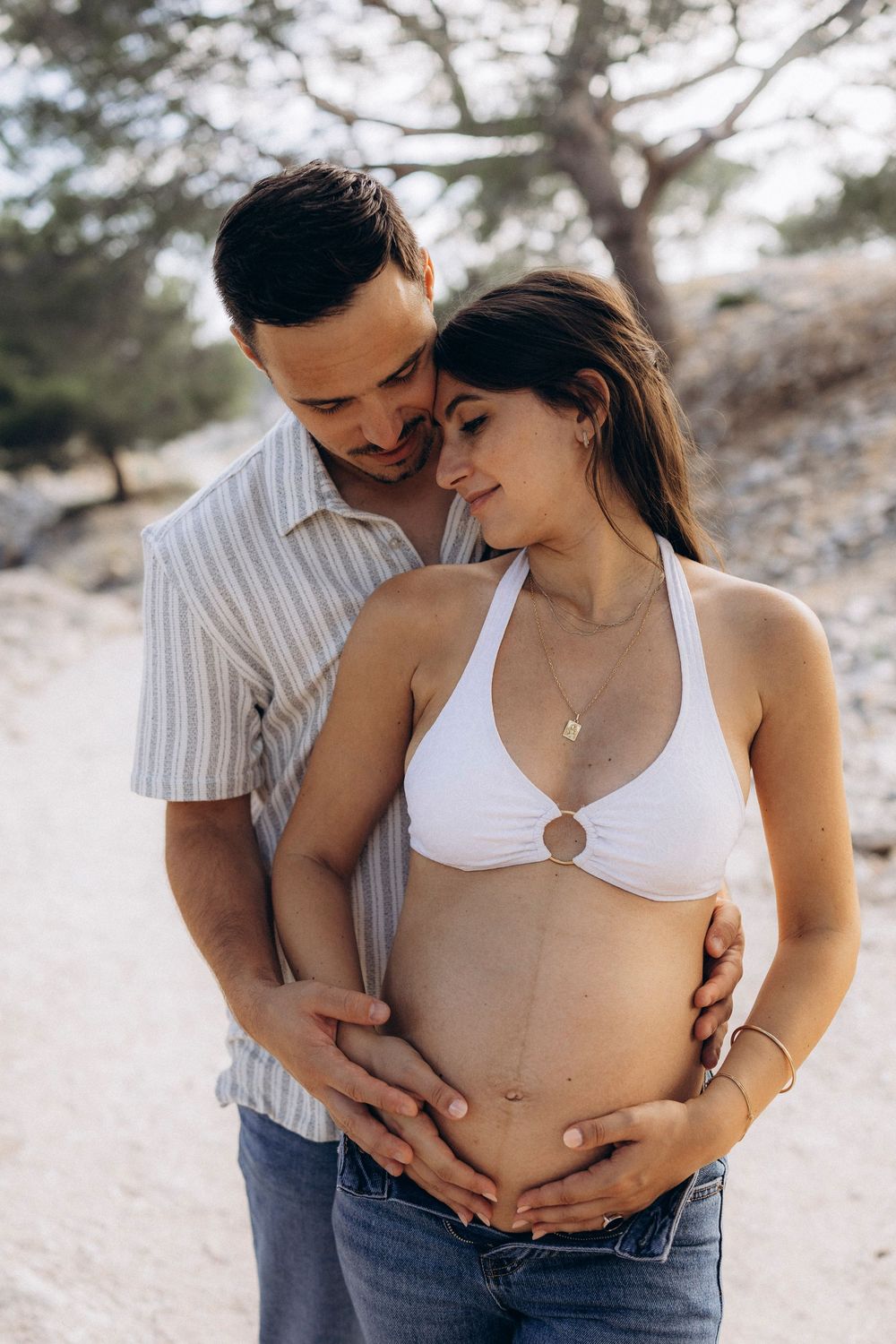 Intimate maternity photo series showing couple embracing on sandy beach in soft natural light.