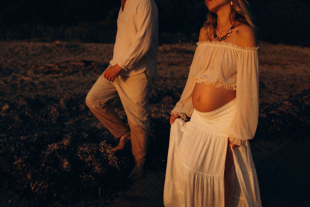 A couple in white clothing poses together at sunset in a rustic outdoor setting.