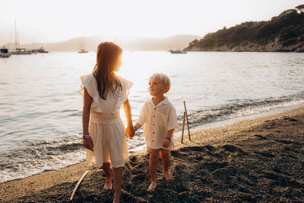 Two people sitting together on a rocky beach at sunset watching the golden light reflect off the ocean waves.