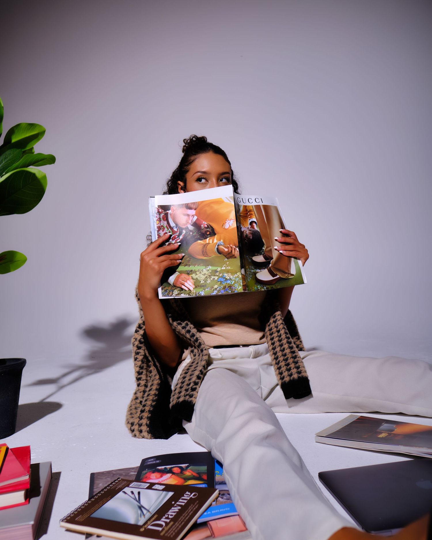 Someone holding magazines while sitting casually surrounded by books and plants.