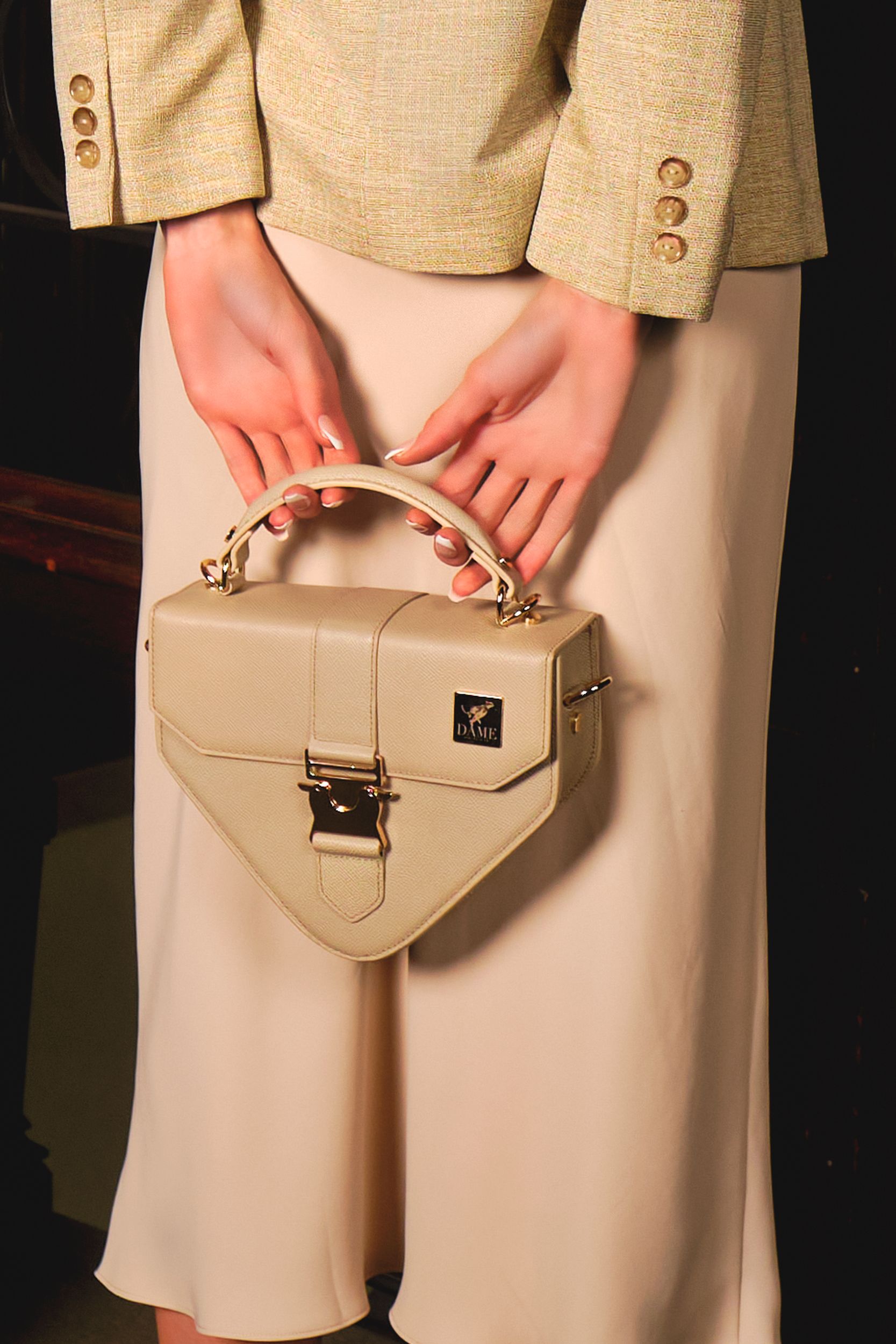 Close-up of beige leather handbag with geometric design held against neutral clothing.