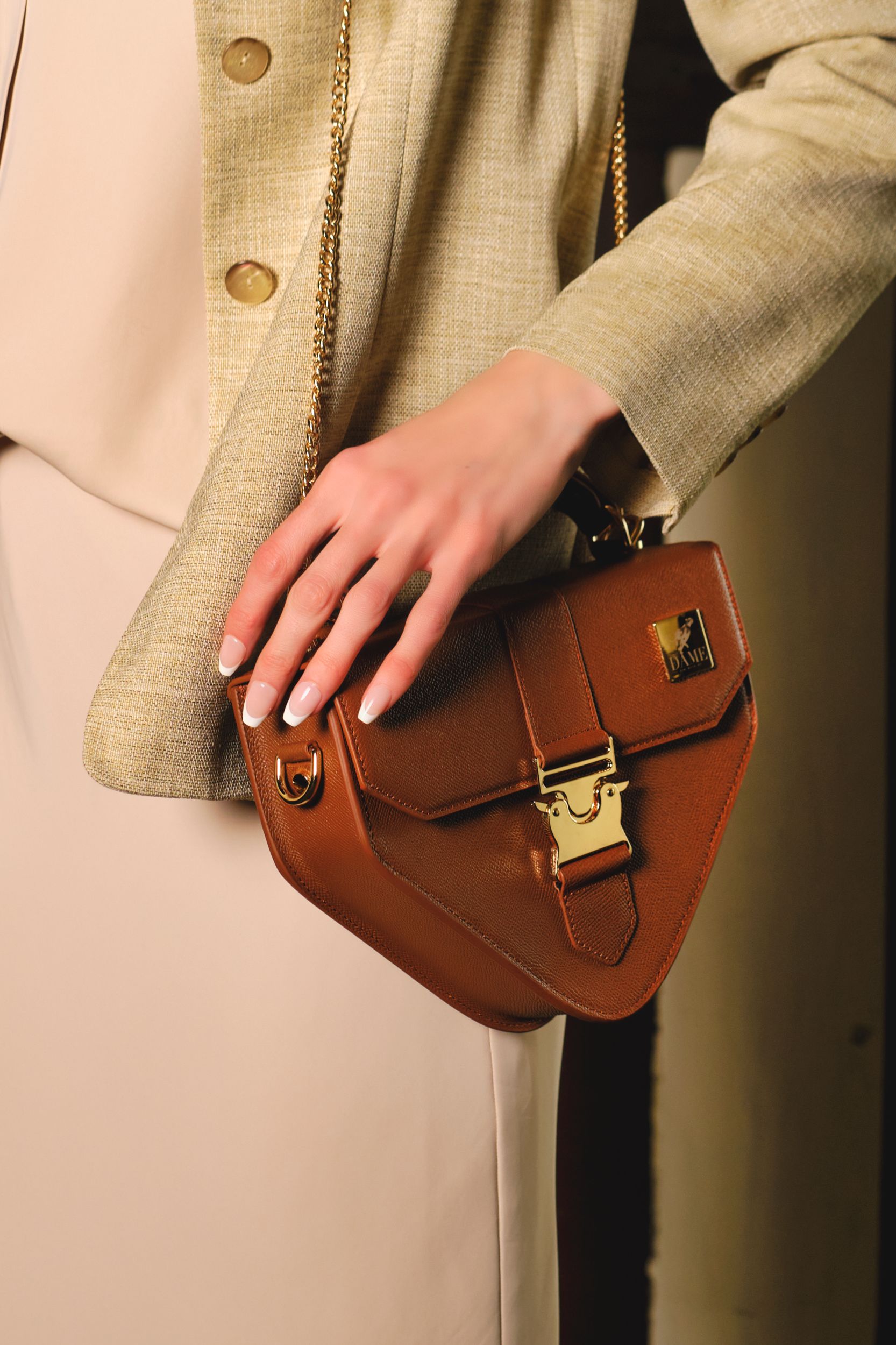 Brown leather crossbody bag with gold hardware shown against beige clothing.